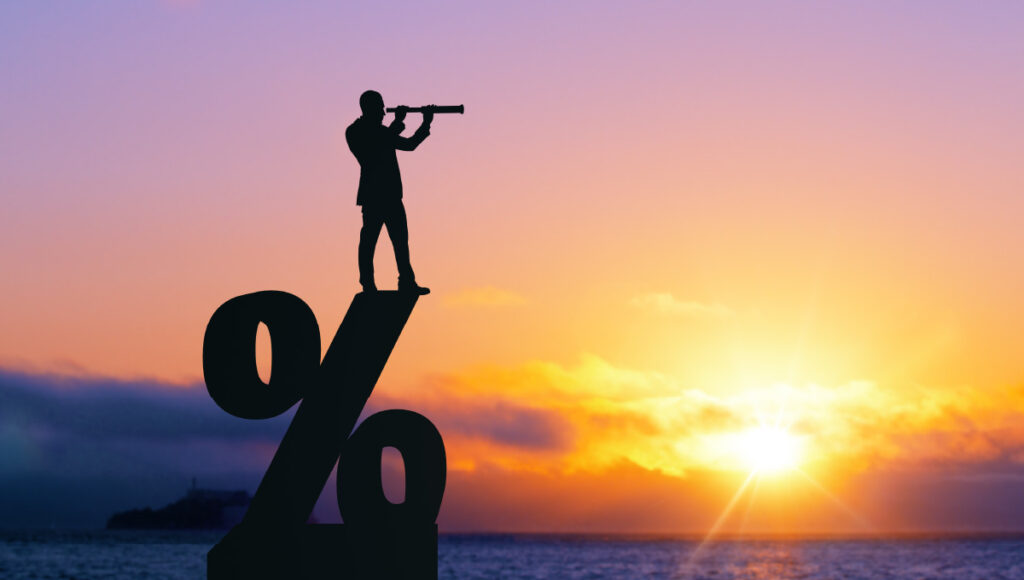 A man with a spyglass standing on a percent sign illustrating he is keeping an eye on rising rates as it pertains to his investment portfolio.