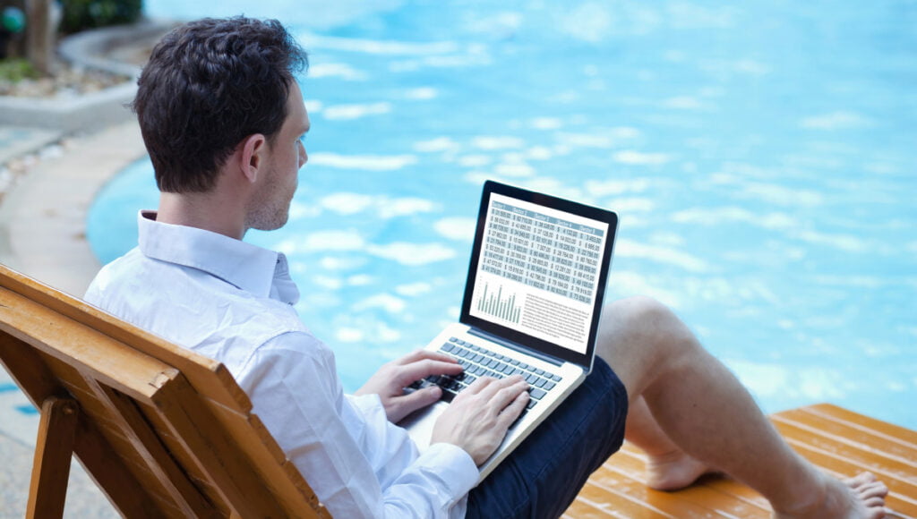 An investor is interpreting stock quotes on his laptop, while sitting next to a swimming pool.