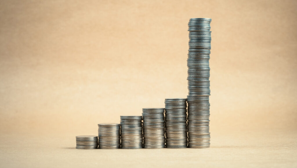Compounding returns represented by a row of coins that gradually gain in height.