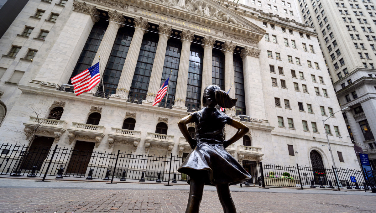 A photo of the New York Stock Exchange with a bronze statue of little girl looking at the building.